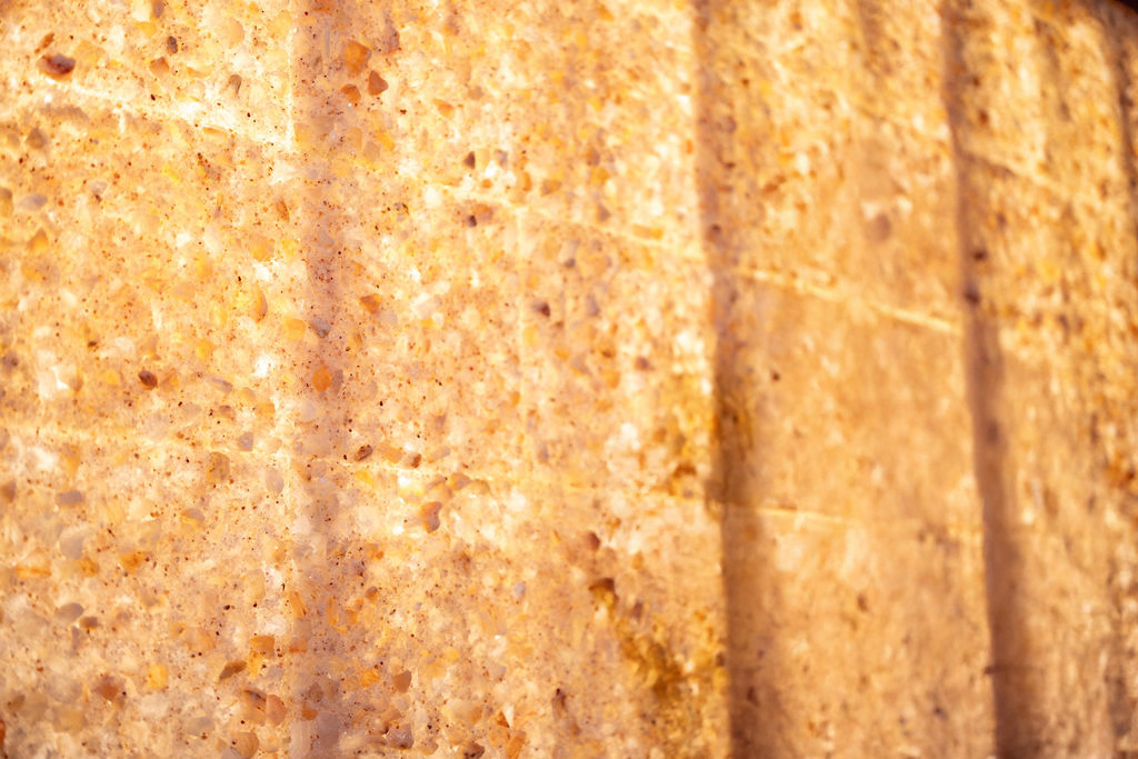Close-up view of a textured, light brown stone or mineral surface with visible grains and vertical lines.